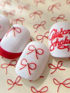 Macro shot of bow nail stickers with red lines, metallic beads, and handwriting design