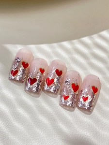 Detail of pink gradient press-on nails with silver foil and red heart glitter accents