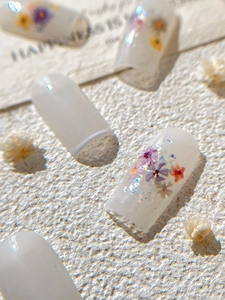 Macro detail of handmade press-on nails with dried flowers and glitter on ivory base