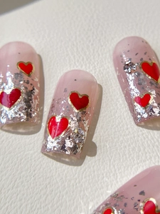 Macro detail of handmade light pink press-on nails with red hearts and silver foil flakes