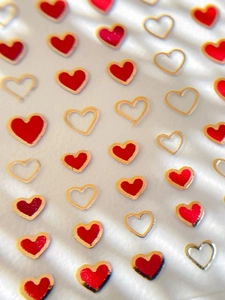 Detailed view of red and gold heart-shaped nail art stickers on a soft white texture