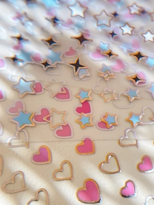 Macro shot of gold-rimmed star and heart nail art stickers on a transparent backing