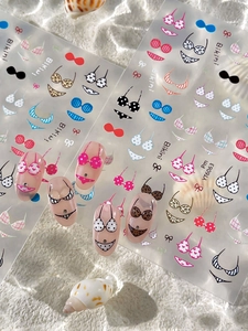 Détail des stickers à ongles motif bikini avec coquillages sur fond de plage d'été