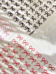 Detail of 3D bow nail stickers in black, white, red, and pink colors for manicure