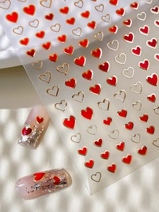 Macro shot of gold and red heart nail art stickers on a silver glitter manicure base