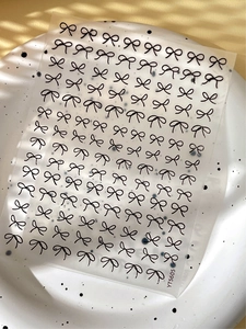 Close-up of black bow embossed nail art stickers on a white textured plate with soft shadows