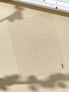 Detail view of white bow relief nail stickers YT5604 on a textured beige background