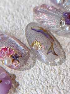 Dettaglio macro di unghie lilla a tema oceano con conchiglie 3D e piccole perle