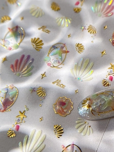 Macro detail of iridescent shell nail stickers with gold foil sea stars and ocean motifs