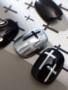 Macro detail of gothic cross nail charms with silver heart relief and black glossy finish