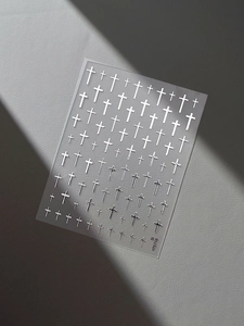 Close-up of metallic silver cross nail art stickers on a textured minimalist background