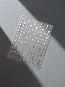 Detailed close-up of golden embossed cross nail art stickers on a transparent sheet