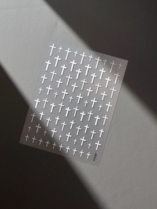 Detailed view of white cross nail art stickers with embossed patterns on grey background