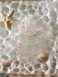 Iridescent starfish and seashell nail stickers with pearls on a sandy ocean backdrop