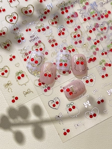 Dettaglio di adesivi per unghie 3D dorati con fragole e ciliegie su unghie finte rosa