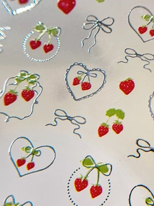 Vista macro di adesivi per unghie 3D con fragole e fiocchi d'argento decorativi