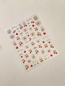 Dettaglio di adesivi per unghie con fragole rosse, fiocchi d'oro e motivi a cuore