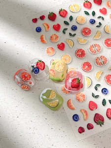 Macro shot of 3D fruit nail art stickers featuring strawberry and orange embossed patterns