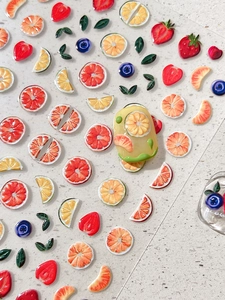 Detail of 3D embossed fruit nail stickers featuring strawberries and oranges on yellow nails