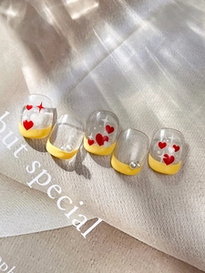 Detailed macro view of French style nail tips with yellow tips and 3D heart charms