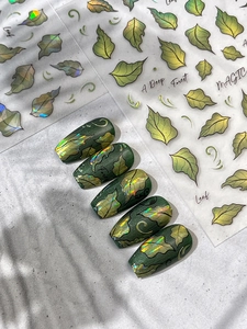 Macro shot of laser leaf nail art stickers with gold foil edges and deep forest aesthetic