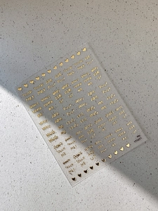 Detail of embossed gold alphabet nail stickers with heart patterns and phrases