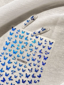 Detail of laser blue gradient butterfly nail stickers with rhinestones on white fabric
