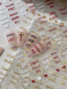 Detail of embossed gold and red nail stickers featuring chic phrases and heart patterns