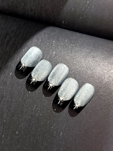 Detail of grey cat-eye nail charms with silver starburst and black French tips
