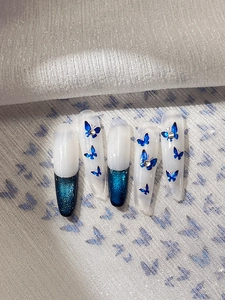 Long almond press-on nails with blue metallic butterfly decals and silver glitter accents