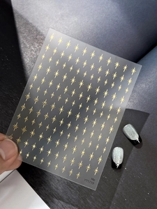 Detailed view of golden starburst nail stickers on dark textured background with application effect