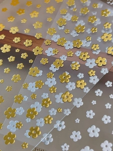 Detail of 3D embossed floral nail art stickers in gold and white on clear sheets