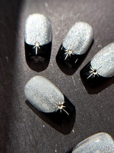 Close-up of square nails with silver glitter, black contrast, and starburst rhinestone design
