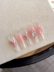 Detail of pink gradient press-on nails with 3D butterfly charms and pearl accents