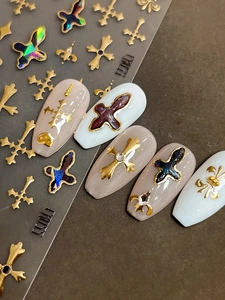 Detailed view of gold cross and fleur-de-lis metallic nail art stickers on fake nails