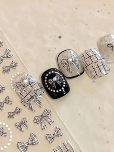 Macro detail of 3D bow and pearl nail stickers with silver glitter and plaid patterns