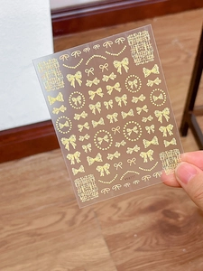 Close-up of golden 3D embossed nail stickers featuring elegant bow and pearl designs