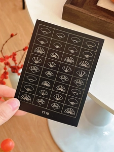 Detailed view of traditional Chinese golden fan nail art stickers on a black card
