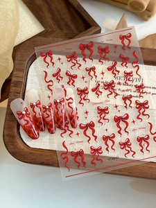Detail of red bow nail stickers with star motifs and gradient faux nails on fabric