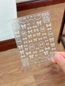 Detail view of 3D embossed bow and pearl necklace nail art stickers in white color