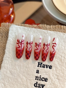 Macro detail of ballet-style long nails with red bows, pearls, and plaid patterns