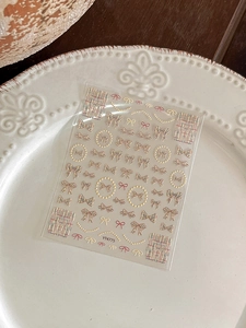 Detail view of embossed bow and pearl nail stickers on a white ceramic plate