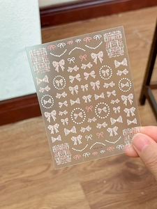 Detail of adhesive nail art stickers featuring pink bows, pearls, and plaid patterns