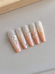 Detail of coffin press-on nails with pink gradient, white wings, pearls and silver chains