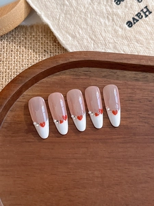 Close-up of French press-on nails with red hearts and pearls on a wooden tray