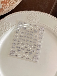 Close-up of bow nail art stickers with pearl details and grey plaid patterns on white plate
