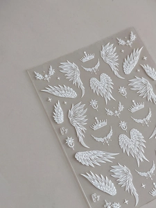 Detail of 5D embossed white wing and crown nail art stickers on a transparent sheet