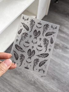 Detail of black gothic nail art stickers featuring wings, crowns and fly text elements