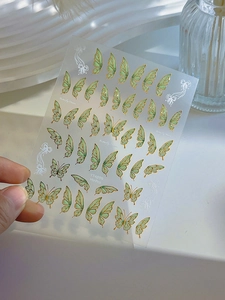 Close-up of butterfly nail stickers with gold foil outlines and light green wing patterns
