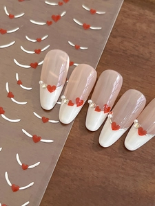 Detail of red heart nail stickers with silver foil wings and pearls on French tips